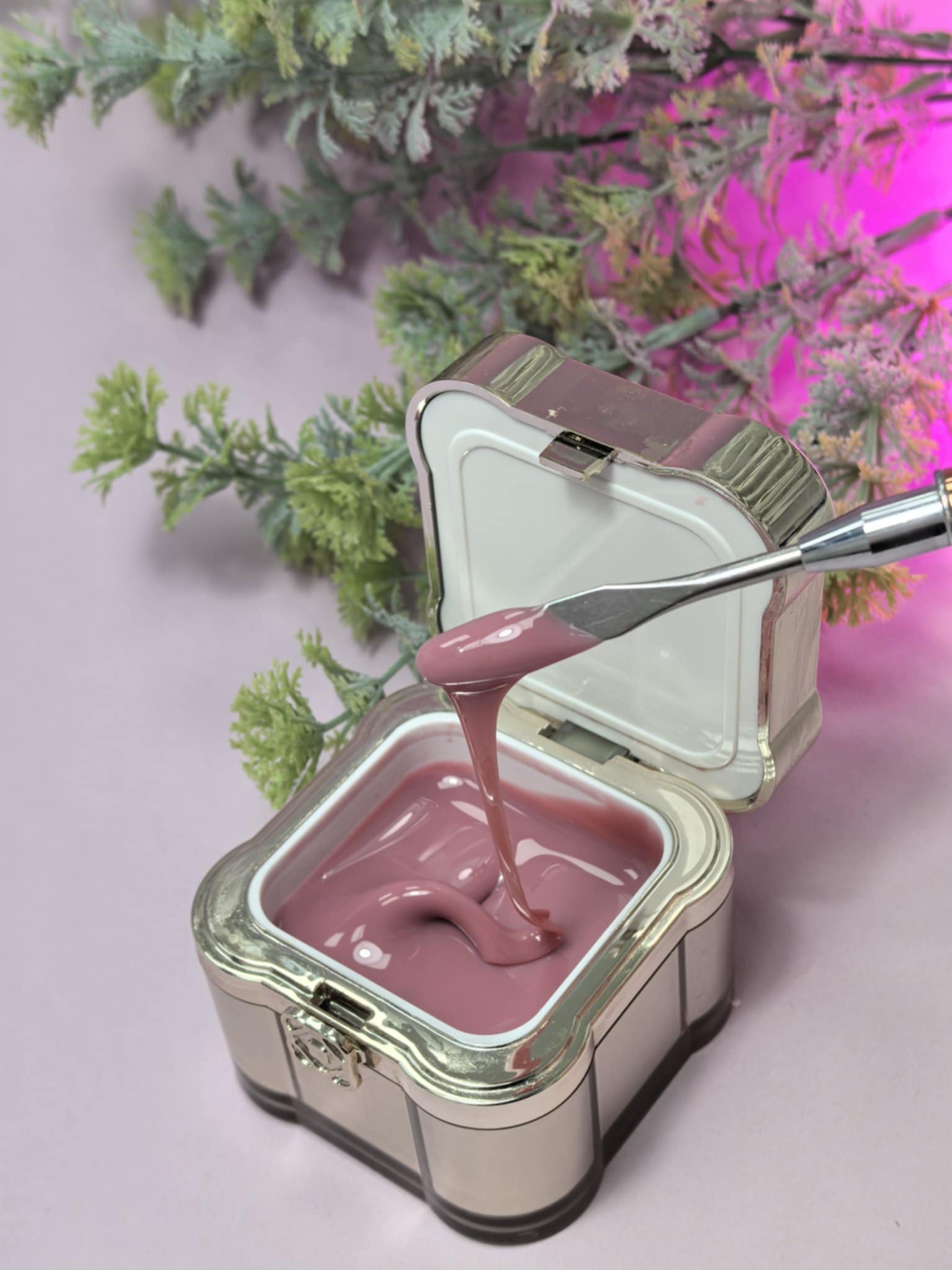 Lemmy Builder Gel 23 - Mocca Mousse in an open container with application tool, surrounded by foliage, showcasing creamy texture.